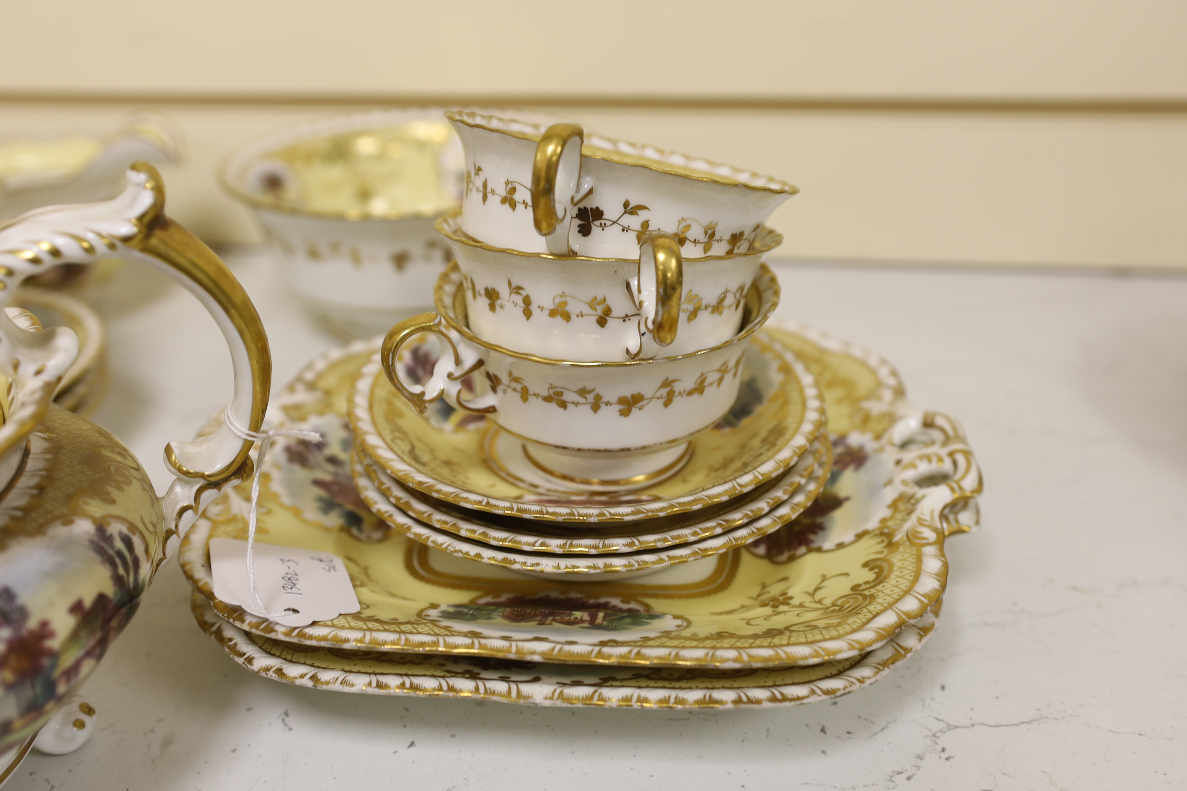 An English porcelain tea set, c.1835-45, including a teapot and cover, sucrier and cover, slops bowl, milk jug, teacups and saucers, two cake plates, each piece painted with buildings in landscapes, yellow ground, patter